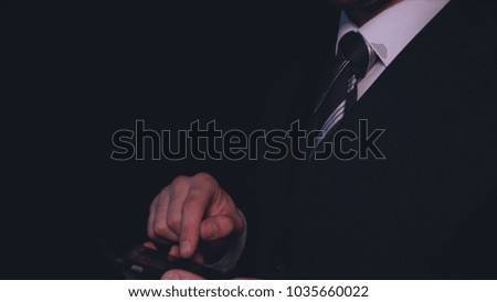 Businessman in suit working on phone, black background.