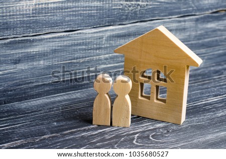 Two people are standing near the house. Wooden figures of persons stand near a wooden house. The concept of a couple in love, cohabitants, parents, buyers and sellers at home. They live in the house.  Royalty-Free Stock Photo #1035680527