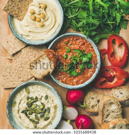 Vegan snack board. Flat-lay of various Vegetarian dips hummus, babaganush and muhammara with crackers, bread and fresh vegetables, top view, square crop. Clean eating, healthy, dieting food concept Royalty-Free Stock Photo #1035688438