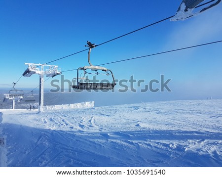 An empty ski lift going up a frozen and snowy mountain with blue sky above