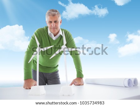 Digital composite of Confident business man looking at models of windmills on the table