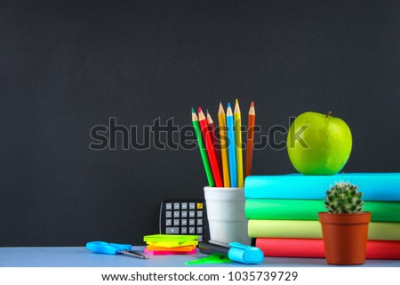 A pile of books and stationery on a chalkboard background. Work desk, education, school
