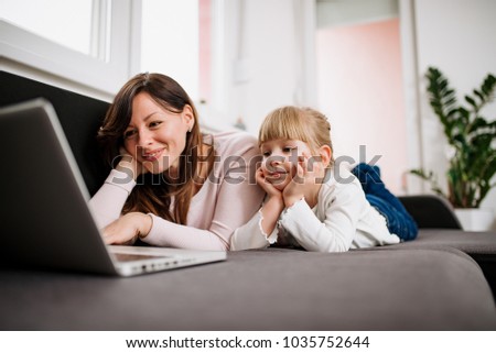 Little girl and her mother watching cartoon on laptop, while lying on couch.