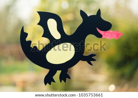 shape of a dragon made with paper as handicraft activity for children and placed on window glass.