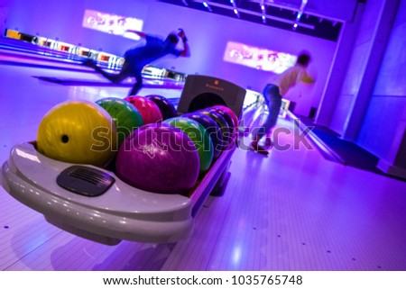 A guy and a girl are playing bowling.  Rack with balls for bowling. 