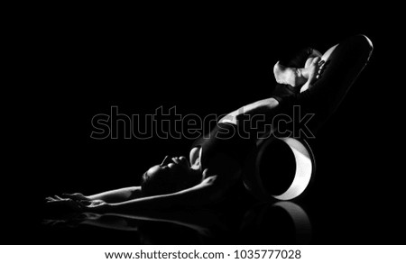 Low key black and white picture of a  girl stretching with a help of yoga wheel 