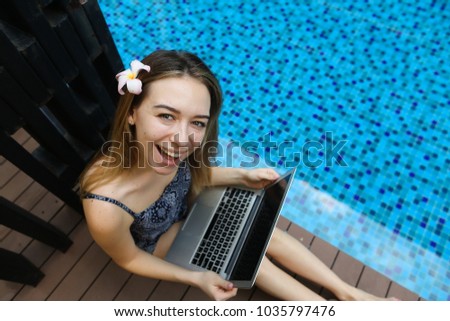 Female woman smilling looking at camera with laptop on background of pool, picture taken from above. girl is using social networks.