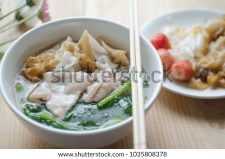 Fried noodle with pork and kale soaked in gravy in white bowl on a wooden table. Thai traditional food and popular menu. Still life image/ selective focus.