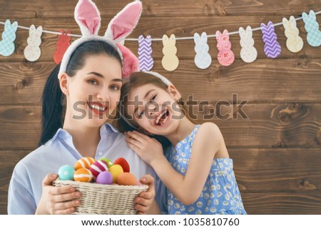Happy holiday! Mother and her daughter with painting eggs. Family preparing for Easter. Cute little child girl is wearing bunny ears.