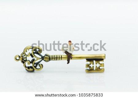 Miniature people: Businessman sitting on key and reading newspaper. Image use for key man, the key to success, business concept.