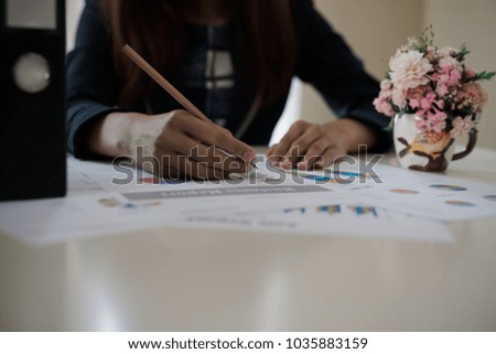 Business woman holding a pencil is working with graph on the desk related to business functions