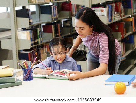 Young mother reading books with  kid at home. Young teacher teaching boy kids at the school. The tutor with young  student in the library 