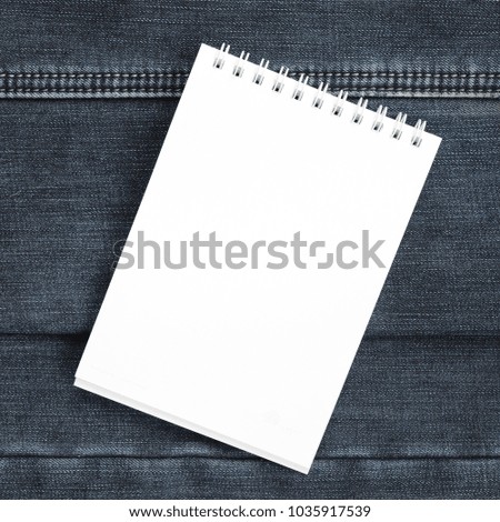 White notebook with clean pages lying on dark blue jeans background. Image with copy space
