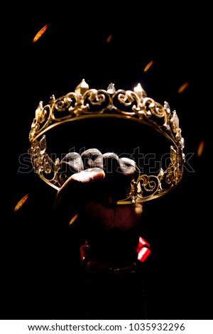hand wearing coral beads clenching a gold crown raised up, with fire raining down from the sky with a black backdrop . Depicting a conquered kings crown after a war antebellum