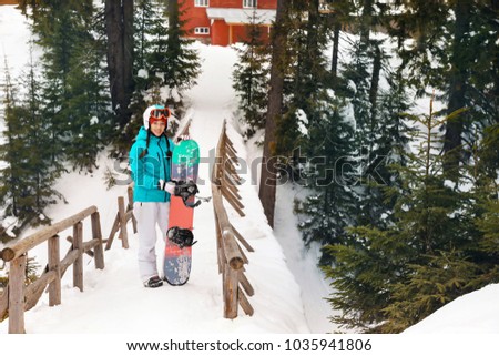 Happy female snowboarder on bridge at snowy resort. Winter vacation
