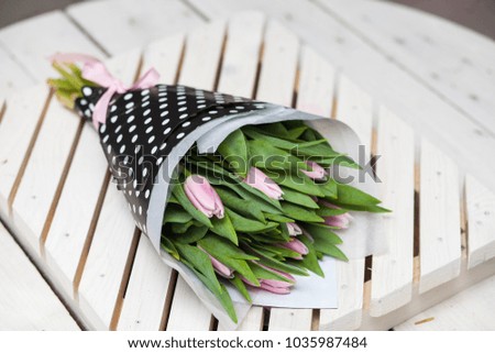 Beautiful spring pink tulips wrapped in stulish paper on a wooden background