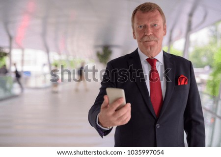 Portrait of handsome senior businessman with mustache exploring the city of Bangkok, Thailand