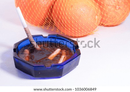 Frozen cigarette in an ashtray and oranges behind it. Health concept.