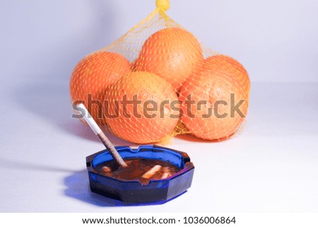 Frozen cigarette in an ashtray and oranges behind it. Health concept.