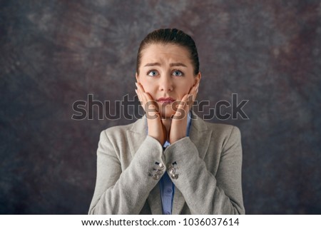 Dismayed upset young woman with her hands to her cheeks staring wide eyed at the camera with a tearful expression over a textured slate background