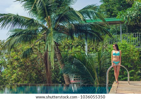 beautiful girl in bikini standing near swimming pool and looking away