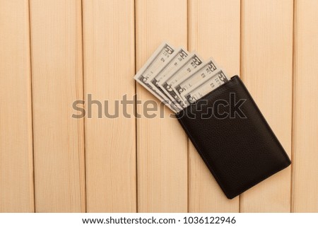 Leather wallet , dollars and coins on the background light wooden table .