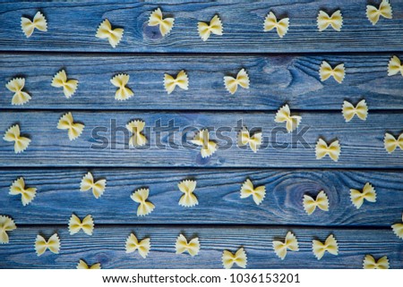 Pasta farfalle is lying on a wooden blue kitchen table  