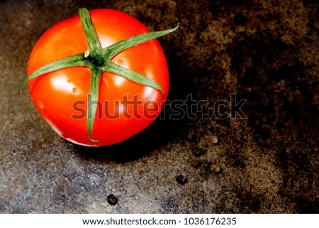 A tomato. Useful tasty vegetable. A fresh ripe tomato in droplets of water and a pea of black pepper on a dark background.