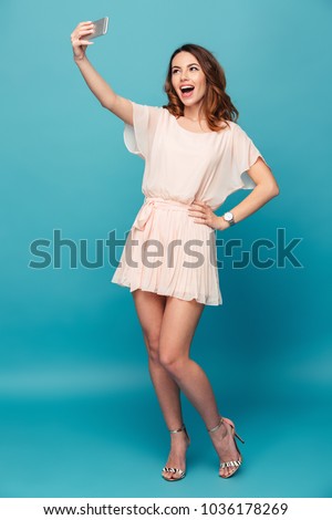 Image of cute pretty young lady isolated over blue background. Looking aside make selfie by mobile phone.