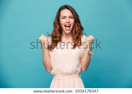Image of excited young lady standing isolated over blue background make winner gesture. Royalty-Free Stock Photo #1036178347
