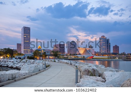 City of Milwaukee skyline. Image of Milwaukee skyline at twilight with city reflection in lake Michigan and harbor pier.