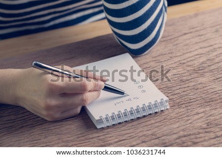Female hand holding pen writing business plan to do list on wood table in vintage color effect, task priority and work or day to day organize.