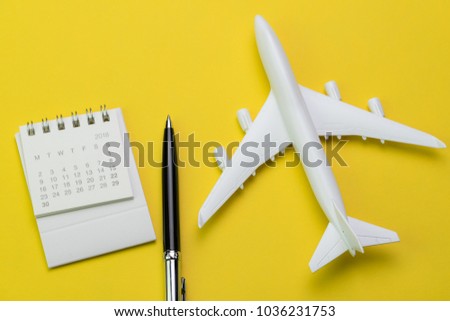 Flat lay of travel and tourism concept, small white clean paper calendar with black pen and toy airplane on vibrant yellow background.