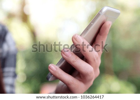 Closeup image of a hand holding , using and looking at smart phone with blur green nature background