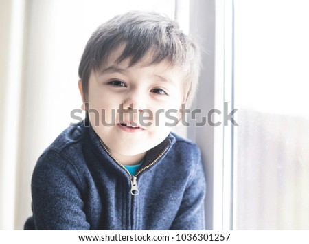 Portrait of Kid boy sitting next to the window and looking at the camera in the sunny day in retro filter, Happy Child relaxing at home