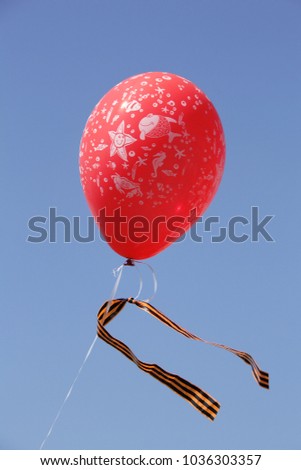 Air balloon with a St. George ribbon tied to it against the background of a cloudless blue sky.