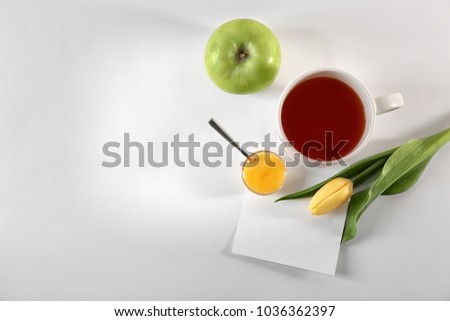 Cup of tea, apple, flower and empty card on table, top view. Tasty breakfast