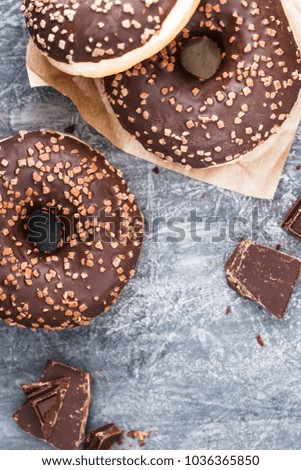 Three chocolate donuts over a grey textured background. Flat lay. Copy space.