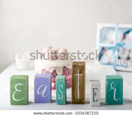 Easter composition with letters on a wooden cubes and easter cake and candles on background. White table and white background. Picture made in high key style. Space for letters.