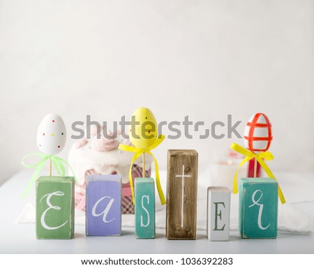 Easter composition with letters on a wooden cubes and easter cake and multi-colored easter eggs on background. White table and white background. Picture made in high key style. Space for letters.