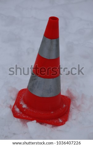 Close up outdoor view of a traffic symbol. Orange and white cone placed on the snow to signal a danger. Abstract image of an isolated colorful plastic element located on a large white natural surface.