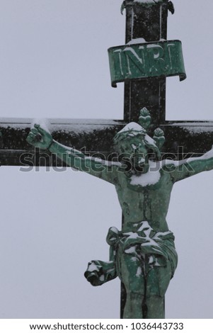 Close up outdoor view of a metallic green cross with jesus christ partially covered by the snow. White snowy sky in background. Isolated religious element. Symbol of faith. Abstract melancholy image.