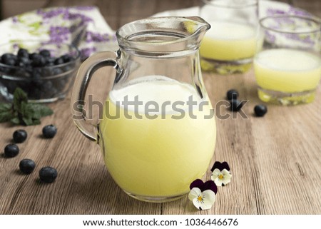 A jug of fresh whey with two glasses of whey and blueberries in the background
