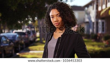 Somber modern African-American woman standing outside in residential area Royalty-Free Stock Photo #1036453303