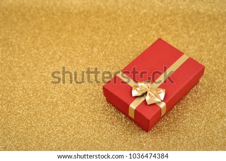 Red gift box stock images. Red gift box with golden bow. Red gift box on a golden background. Golden holiday background with gift. Golden festive background with copy space for text