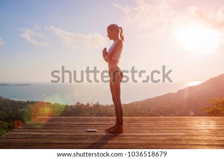 woman doing yoga salutation to the sun Surya Namaskar exercises sequence asan at orange sun up morning high outdoor beautiful view of the island sky sea outside. Namaste hands full body place for text Royalty-Free Stock Photo #1036518679