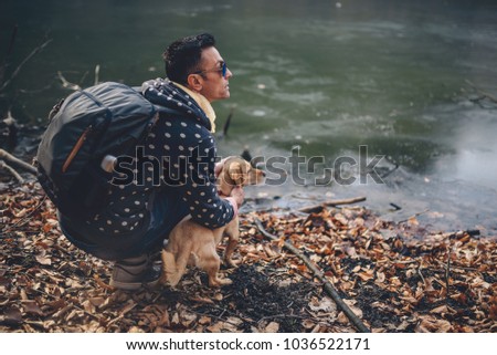 Men wearing backpack resting by the frozen lake with small yellow dog
