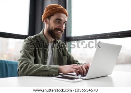 Freelancer hipster typing on keyboard using laptop computer in loft office. Smiling bearded student learning languages at library, planning project. Portrait of skilled copywriter at workplace Royalty-Free Stock Photo #1036534570