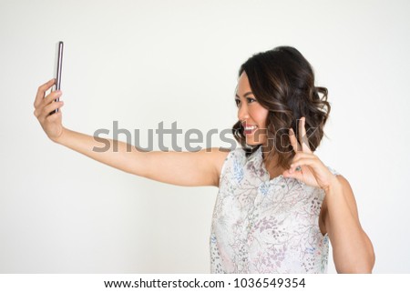Closeup portrait of smiling young beautiful dark-haired woman taking selfie photo and showing victory sign. Selfie photo concept. Isolated side view on white background.