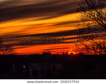 Gorgeous vivid and saturated painted sky sunset in Milwaukee with layered orange, yellow and red colored clouds with silhouettes of trees and buildings in the foreground at dusk.